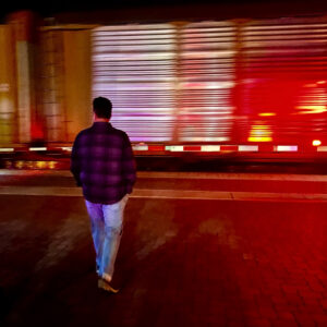 man in front of train tracks with train wizzing by